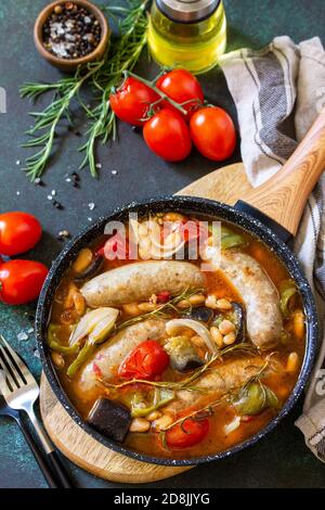 Ragoût les saucisses fumées avec des haricots, des légumes et de la sauce tomate dans la casserole sur un comptoir en pierre. Banque D'Images