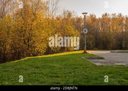 Panneau routier sur le fond d'une forêt dorée dans un cercle de nombre rouge, prairie d'automne, herbe verte lumière du soleil route asphaltée à l'ombre Banque D'Images