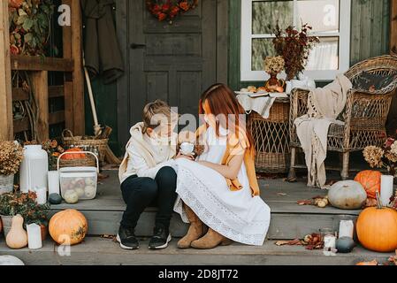 les enfants un garçon et une fille avec leur chien de pirochon dans des masques protecteurs sur le porche de l'arrière-cour décoré avec des citrouilles en automne, le concept de la Banque D'Images