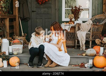 les enfants un garçon et une fille avec leur chien de pirochon dans des masques protecteurs sur le porche de l'arrière-cour décoré avec des citrouilles en automne, le concept de la Banque D'Images