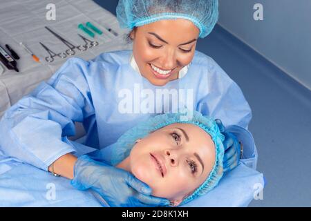 Chirurgien en plastique vérifiant le visage d'une femme d'âge moyen avant une chirurgie esthétique Banque D'Images