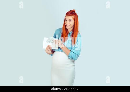 Jeune femme élégante dans l'espérance ayant enveloppe avec l'argent pour bébé recherche heureux isolé sur fond bleu clair. J'ai reçu ma maternité de départ b Banque D'Images