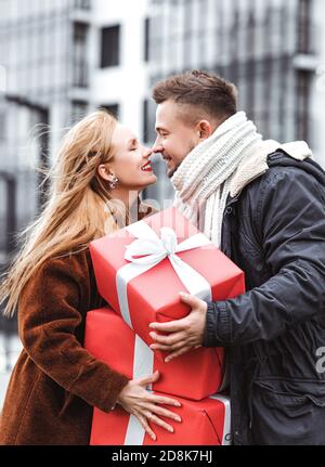 Couple d'amour échangeant des cadeaux à l'extérieur. Surprise romantique pour Noël. Grandes boîtes rouges cadeaux dans les mains Banque D'Images