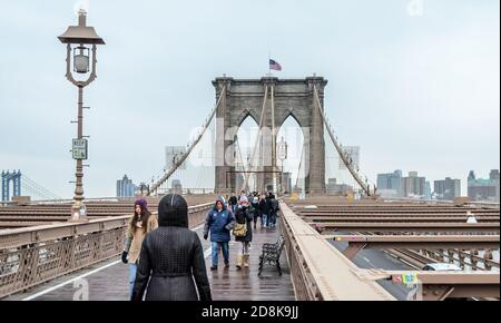 Personnes marchant sur le pont de Brooklyn à Manhattan lors d'un jour de pluie d'hiver. Bâtiments en arrière-plan. New York, États-Unis. Banque D'Images