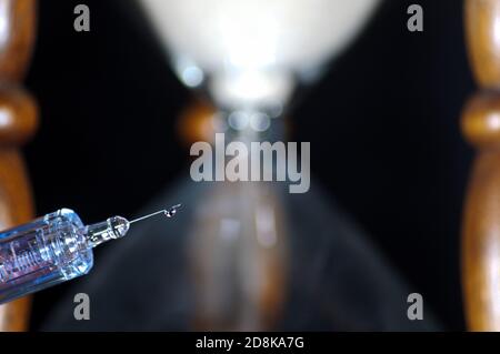 Goutte de vaccin de médecine liquide provenant d'une seringue aiguille hypodermique, avec sablier flou dans le fond Banque D'Images