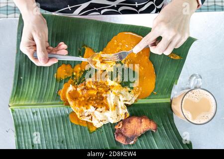 Personne mangeant le roti canai ou le paratha avec le curry sur la feuille de banane avec le thé tarik ou le thé au lait. Banque D'Images