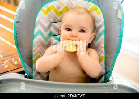 Un portrait de la jeune fille heureuse de bébé en chaise haute mangez des biscuits Banque D'Images