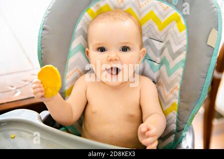 Un portrait de la jeune fille heureuse de bébé en chaise haute mangez des biscuits Banque D'Images