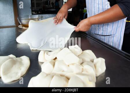 Gros plan des mains de femme pétriant la pâte Roti avec de l'huile sur la table en acier inoxydable. Flou de mouvement. Banque D'Images