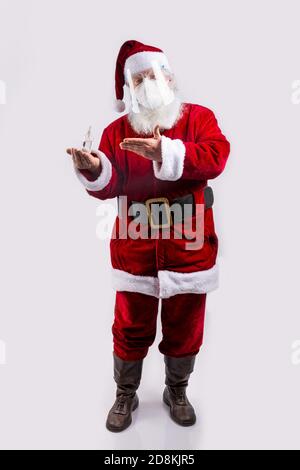 Le Père Noël porte un masque, pointant une bouteille de gel hydroalcoolique sur fond blanc Banque D'Images
