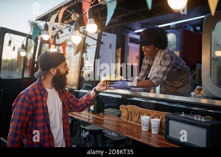 jeune beardy hipster prenant le sandwich pour aller de femme polie employé dans le service de restauration rapide Banque D'Images