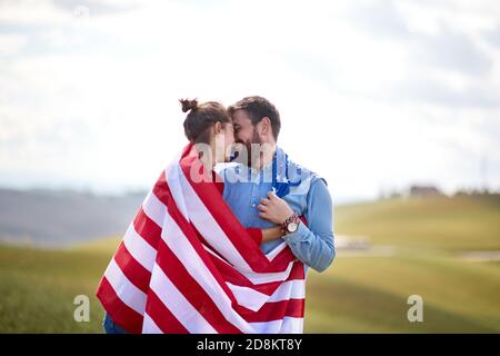 Un couple dans des moments d'amour vêché par le drapeau américain à un pré sur une belle journée ensoleillée. Concept d'élection, de campagne, de liberté Banque D'Images