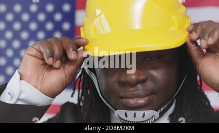 Un ingénieur portant un casque de sécurité avec un drapeau américain en arrière-plan tout en souriant à Camera. - gros plan. Photo de haute qualité Banque D'Images