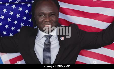 Portrait, jeune homme noir afro-américain en tenue de cérémonie avec badge usa sur la poitrine tenant le drapeau usa. Photo de haute qualité Banque D'Images