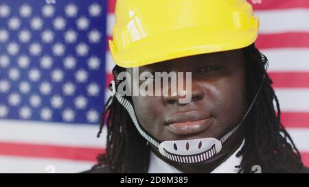 Un ingénieur portant un casque de sécurité avec un drapeau américain en arrière-plan tout en souriant à Camera. - gros plan. Photo de haute qualité Banque D'Images