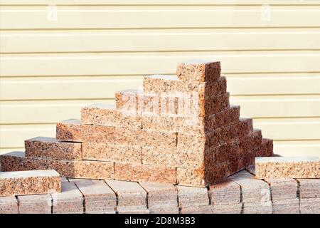 Blocs de granit rouge sculptés et soignés empilés à l'extérieur lors d'une journée ensoleillée sur un fond de mur de parement jaune rayé, espace de copie. Banque D'Images