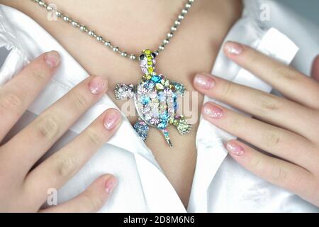 magnifique pendentif tortue sur une chaîne sur le cou de l'adolescent. jeune fille montrant son accessoire étincelant. mains parfaitement entretenues. tortue de pierre précieuse brillante. Banque D'Images