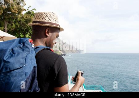 Portrait de l'arrière de l'homme de voyage afro-américain avec sac vue sur le téléphone portable au bord de la mer Banque D'Images