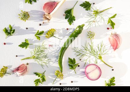 Poivrons chauds verts, ail et oignon rouge avec herbes sur une assiette blanche. Modèle pour une recette. Arrière-plan d'une surface. Banque D'Images