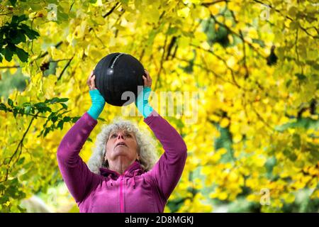 Une femme de ses années 60 levant des poids à l'extérieur pendant l'automne. Banque D'Images