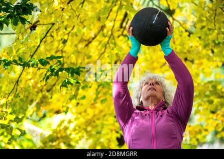 Une femme de ses années 60 levant des poids à l'extérieur pendant l'automne. Banque D'Images