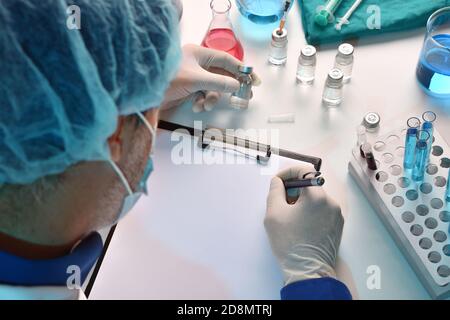 Le personnel de santé ayant des flacons sur la table écrit dans un dossier dans la salle de laboratoire. Composition horizontale. Vue en hauteur. Banque D'Images
