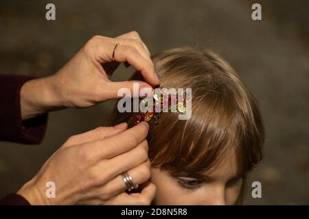 Les mains des femmes d'une mère ou d'un soignant attacher soigneusement une pince à cheveux sur les cheveux d'une petite fille à l'extérieur. Accessoires pour cheveux Banque D'Images