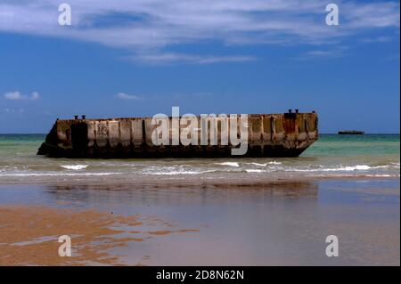 A marée basse à Arromanches, Calvados, Normandie, France, Les gens peuvent marcher jusqu'au bord de l'eau sur la « Gold Beach » de la Seconde Guerre mondiale pour atteindre - mais pas entrer - des sections en béton précoulées de Port Winston ou de Mulberry Harbour B. c'était le port portable préfabriqué de 600,000 tonnes remorqué sur la Manche, Assemblé au large, puis utilisé pendant 10 mois après l’invasion du jour J de l’opération Overlord, le 6 juin 1944, pour atterrir 2.5 millions de troupes britanniques et canadiennes, un demi-million de véhicules et quatre millions de tonnes de fournitures. Banque D'Images