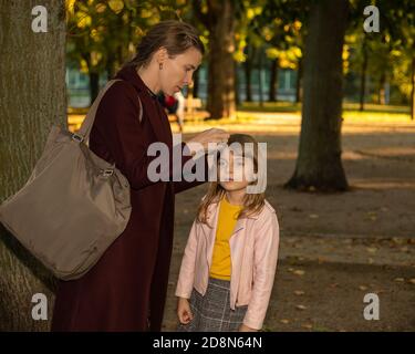 Les mains des femmes d'une mère ou d'un soignant attacher soigneusement une pince à cheveux sur les cheveux d'une petite fille à l'extérieur. Accessoires pour cheveux Banque D'Images