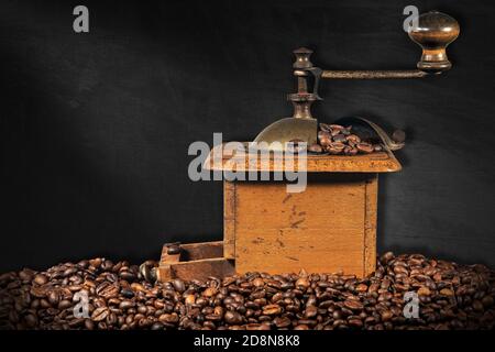 Ancien moulin à café manuel en métal et en bois avec grains de café rôtis et fond noir vide. Banque D'Images