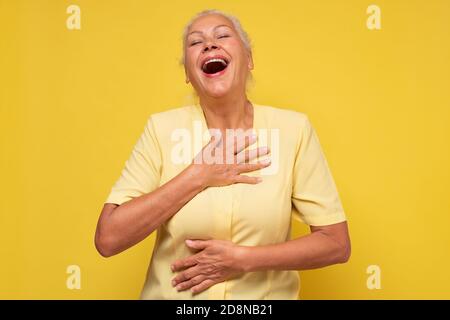 Femme âgée souriant gentiment en riant à la caméra sur le mur jaune. Banque D'Images
