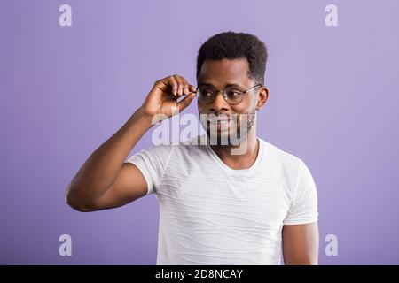 L'Afrique dans les verres joyeux gars habillé en blanc t shirt smiling ayant bonne humeur de toucher le menton tout en se posant en studio sur fond violet. Soins du visage Banque D'Images