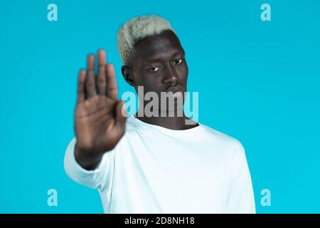 Portrait d'un homme afro-américain sérieux montrant le rejet du geste par le signe de la paume d'arrêt. Guy isolé sur fond bleu. Banque D'Images