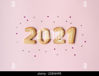 Biscuits de pain d'épice sous forme de nombres, pain d'épice nouvel an 2021 sur fond rose. Vue de dessus. Décoration de Noël confetti étoiles. Banque D'Images