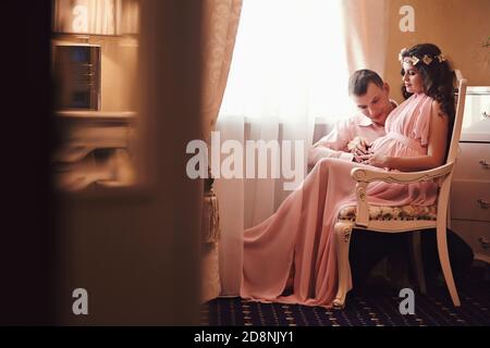 femme enceinte et homme en posant dans un intérieur classique par la fenêtre. en attendant un bébé. grossesse. Banque D'Images