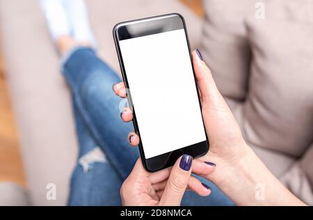 Un smartphone entre les mains d'une femme qui se trouve sur le canapé. Les mains utilisent un smartphone. Banque D'Images