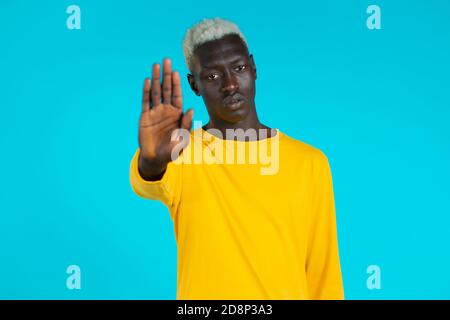 Portrait d'un homme afro-américain sérieux montrant le rejet du geste par le signe de la paume d'arrêt. Guy isolé sur fond bleu. Banque D'Images