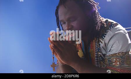 homme noir africain en robe traditionnelle priant avec rosaire. Photo de haute qualité Banque D'Images