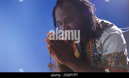 homme noir africain en robe traditionnelle priant avec rosaire. Photo de haute qualité Banque D'Images