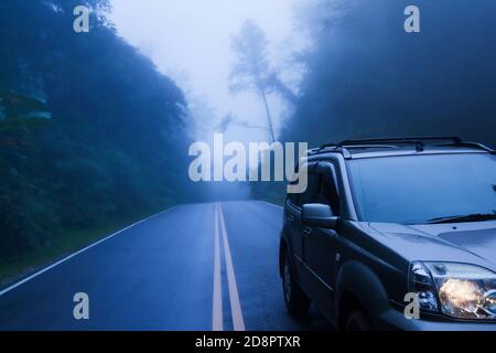 Vue latérale avant d'une voiture SUV argentée sur une route de montagne, parking de la voiture SUV argentée sur le bord de la route dans la brume bleue. Mise au point sélective. Banque D'Images