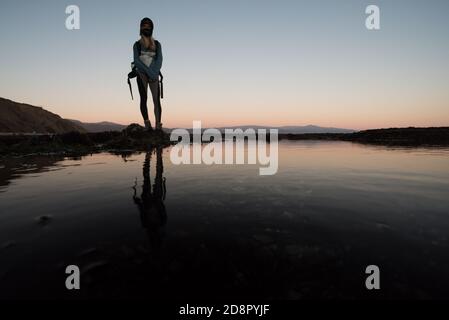 Une femme se tenant au-dessus de la colonne de marée de pointe piscines en Californie en fin de soirée comme le soleil se couche. Banque D'Images