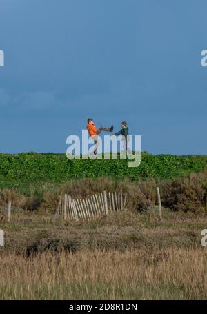 deux jeunes garçons jouent à la bagarres et à coups de pied élevés sur un promenez-vous dans les puits le long de la mer sur la côte de norfolk Banque D'Images