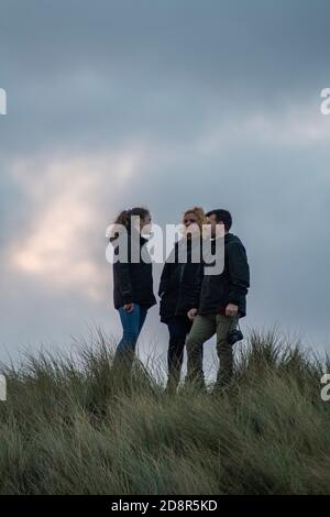 trois personnes ou amis qui parlent en groupe lors d'une promenade sur la côte nord de norfolk ou dans la campagne, le soir d'automne, dans un ciel nuageux et orageux. Banque D'Images