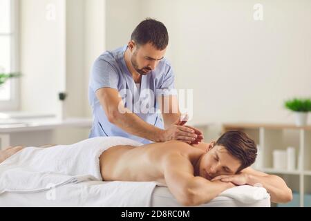 Masseur sérieux faisant un massage relaxant du dos pour le jeune homme utilisant Technique de tapotage Banque D'Images