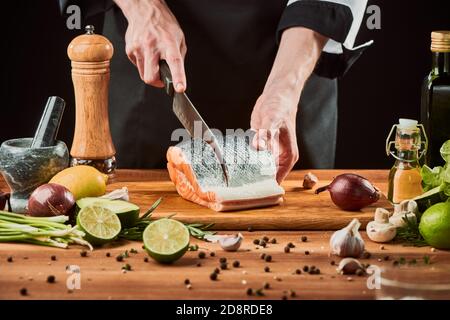 Le chef coupe le filet de saumon dans des steaks sur une planche de bois Banque D'Images