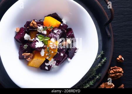 Concept alimentaire salade de betteraves rôties et de butternut avec fromage de chèvre dans un bol en céramique blanc sur fond noir avec espace de copie Banque D'Images