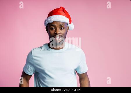 Beau barbu sérieux african american man wearing Santa hat, rouge blanc t shirt, looking at camera avec calme, confiant, isolé des expressions Banque D'Images