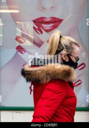 Une femme portant un masque de visage se promène devant la fenêtre du magasin de la barre à ongles dans le centre-ville d'Airdrie pendant la pandémie du coronavirus, en Écosse, au Royaume-Uni Banque D'Images