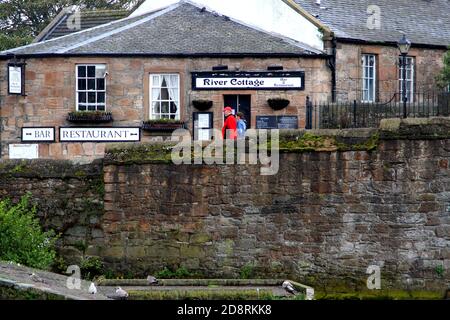 Ayr, Ayrshire, Écosse, Royaume-Uni . Photographie de rue franche autour d'Ayr. Un couple sur le pont passe devant un café appelé River Cottage Banque D'Images