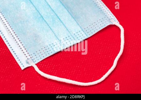 Fragment de masque médical bleu sur fond rouge vif de tissu non tissé. Vue rapprochée du concept de médecine coronavirus pandémique covid-19 disea Banque D'Images